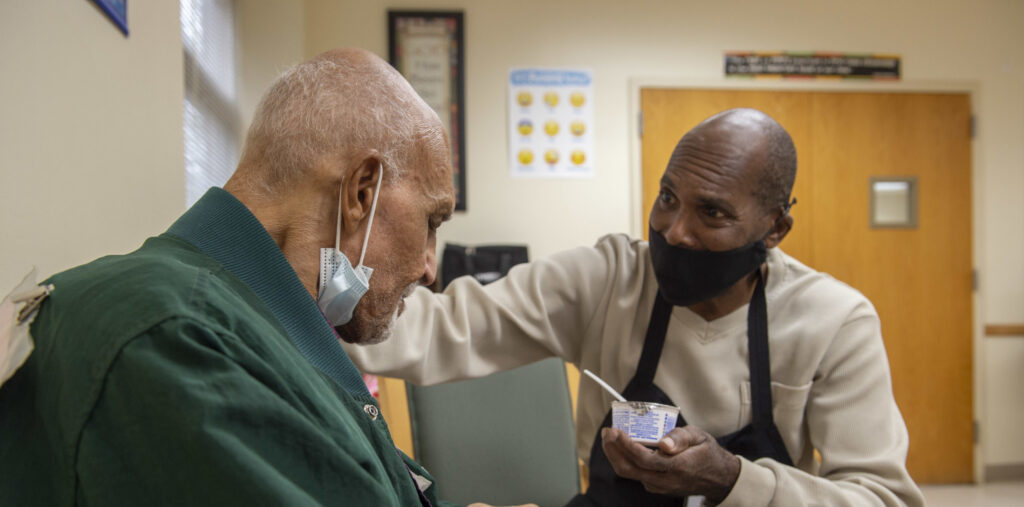 Catholic Charities employee holding a yogurt container with a spoon helping and older man