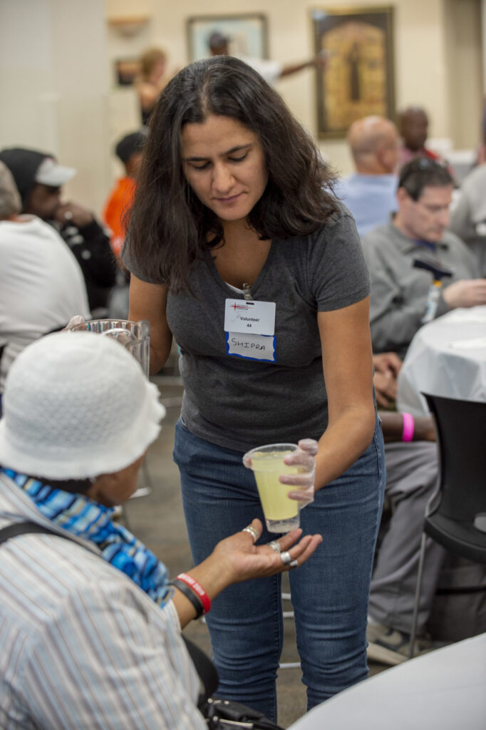 Volunteer handing a drink to a person sitting down.