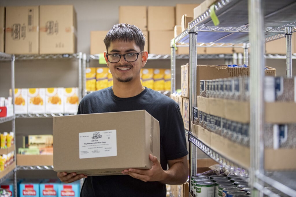 student volunteer Christian Flores holding a box inside food pantry