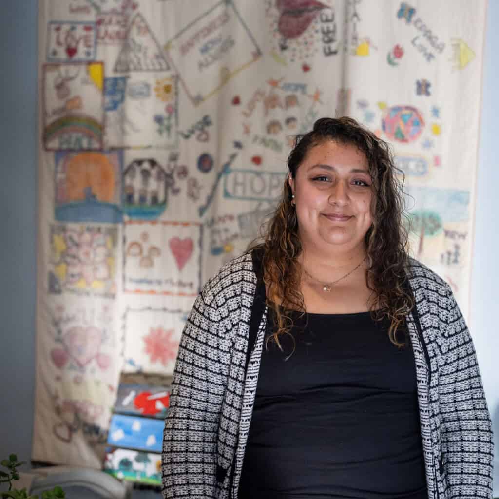 Woman standing in front of a handmade quilt at the House of Good Shepherd